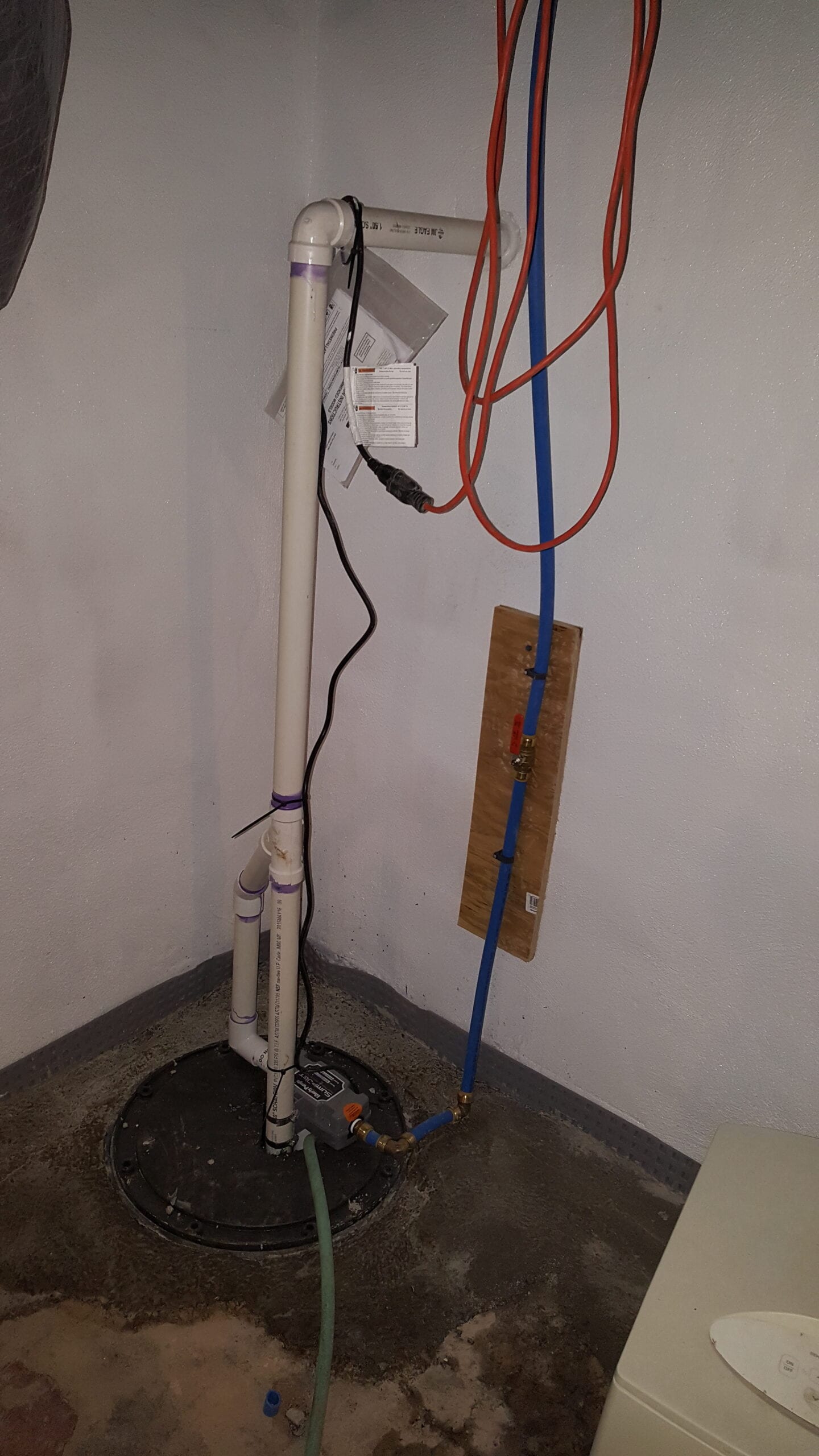 Sump pump installation in a basement with sealed basin, PVC discharge piping, and water line setup.