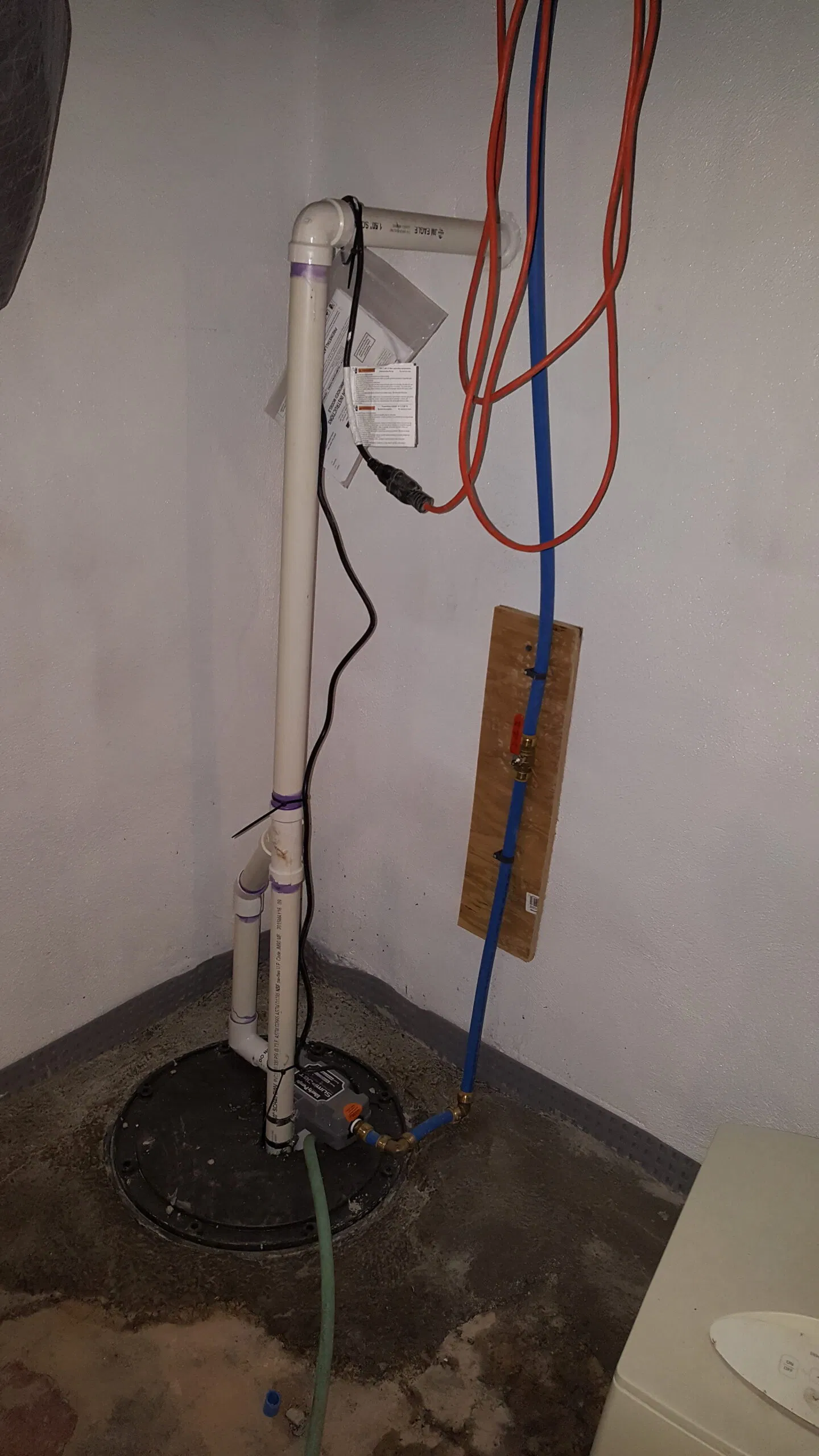 Sump pump installation in a basement with sealed basin, PVC discharge piping, and water line setup.